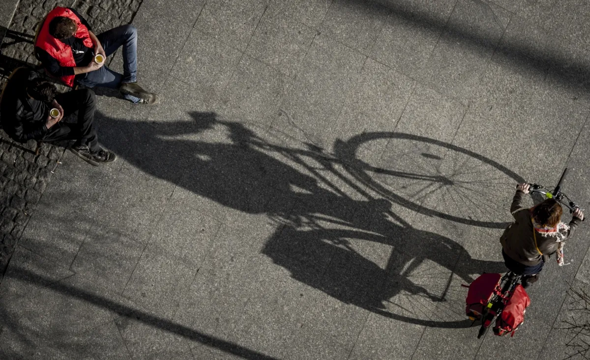 Long bicycle shadow crossing pavement beside a pedestrian's legs